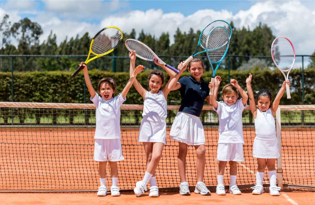 bambini in un campo da tennis con le braccia alzate