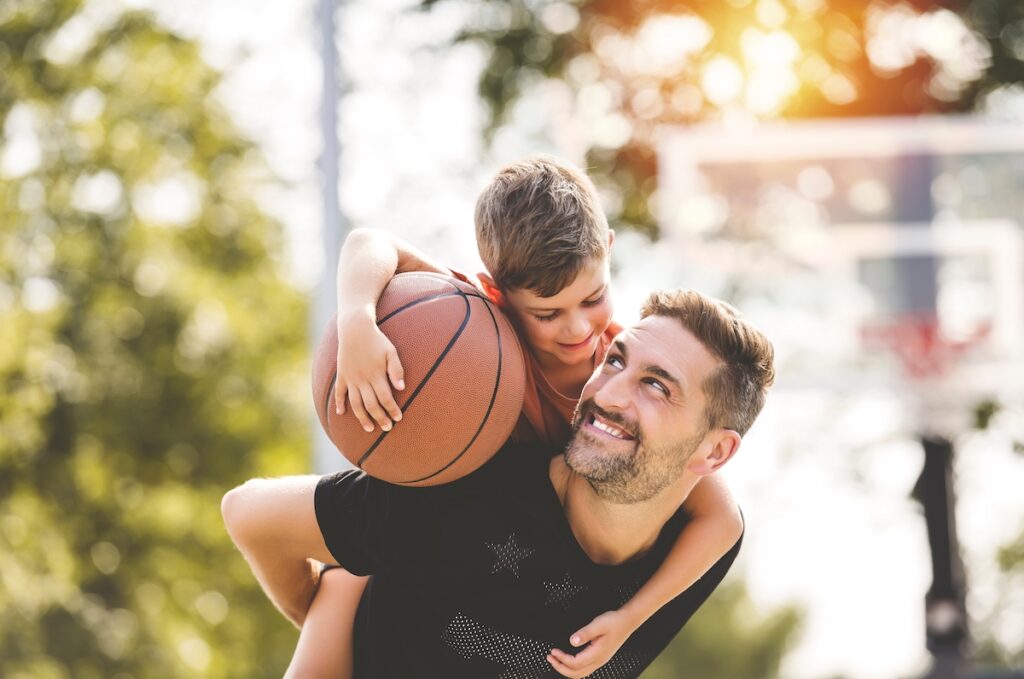 genitore con bambino sulla schiena che tiene in mano una palla da basket