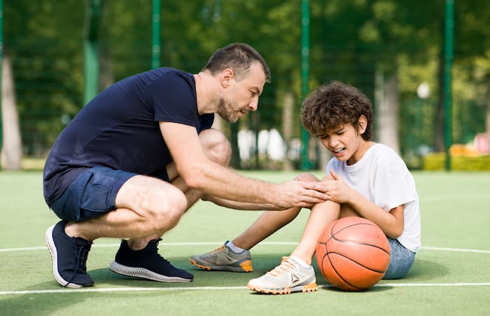 Padre che consola il figlio infortunato durante una partita di basket all&rsquo;aperto